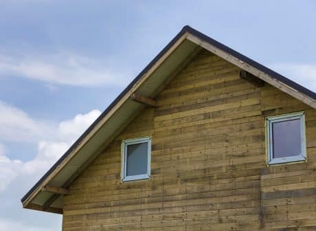 Close-up detail new house top of wooden planks and boards with two narrow plastic attic windows on bright blue sky copy space background. Real estate property and professional construction concept.