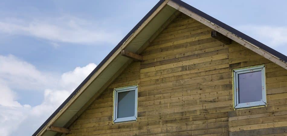 Close-up detail new house top of wooden planks and boards with two narrow plastic attic windows on bright blue sky copy space background. Real estate property and professional construction concept.