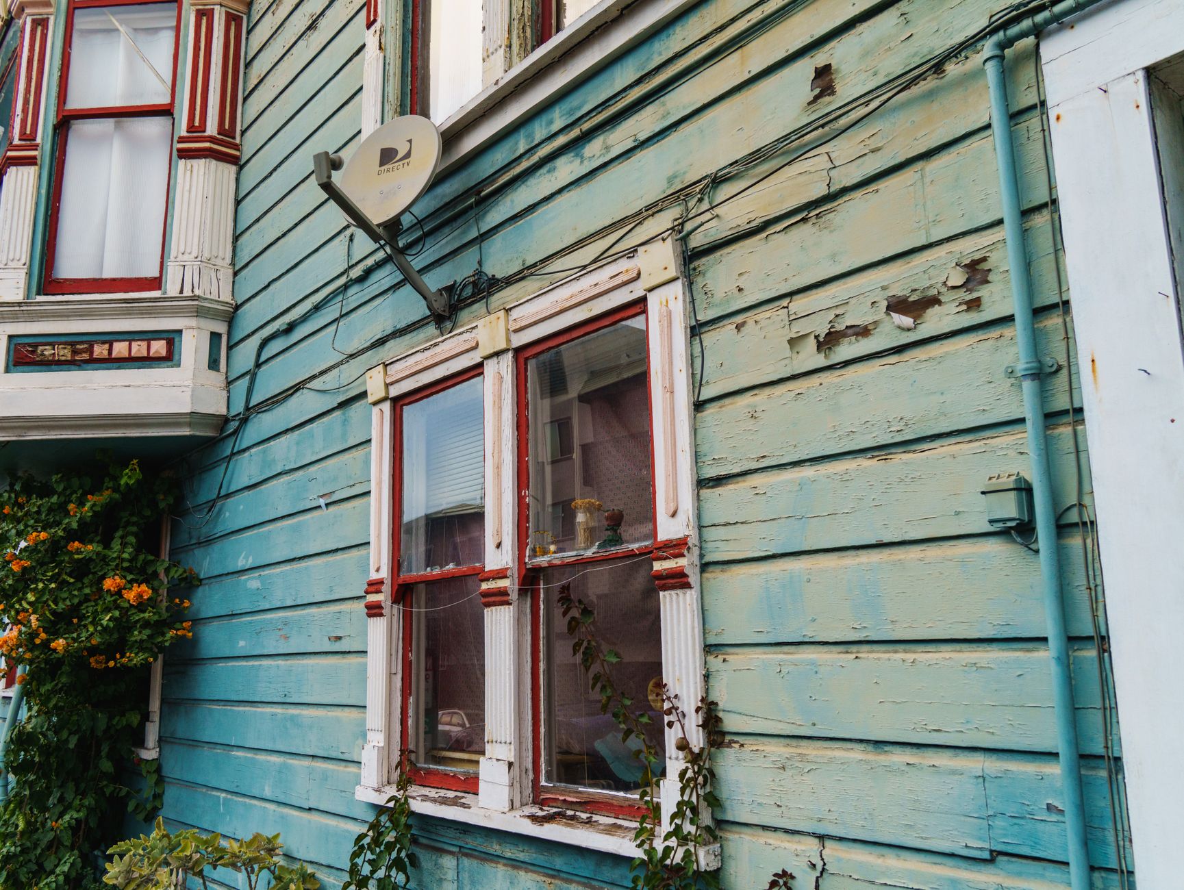 Home exterior siding with peeling paint, warped panels, and water staining indicating moisture damage behind the siding