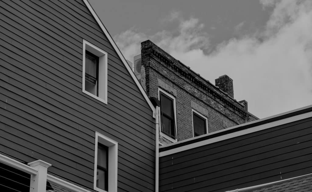 Painted lap siding on a gabled house beside an older brick building, as on tight New Orleans lots