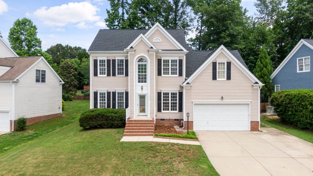 Two-story house with pale vinyl lap siding and black shutters, like many Mandeville and Covington homes