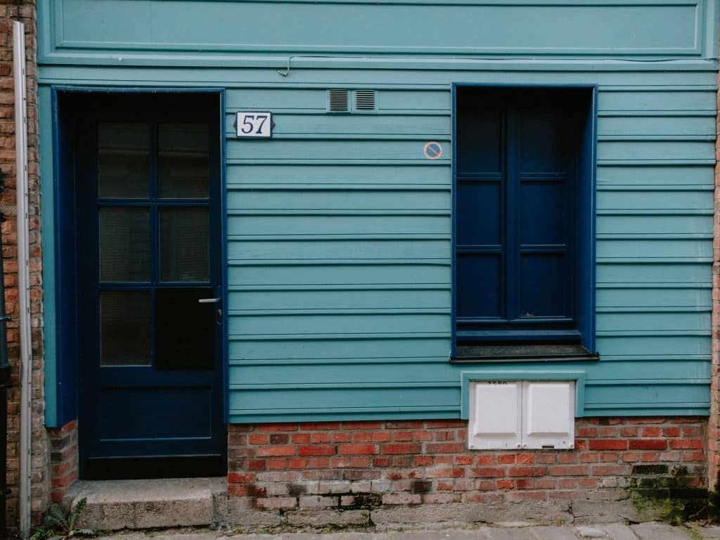Teal wood siding and a dark front door above an old brick foundation, for Gretna homeowners